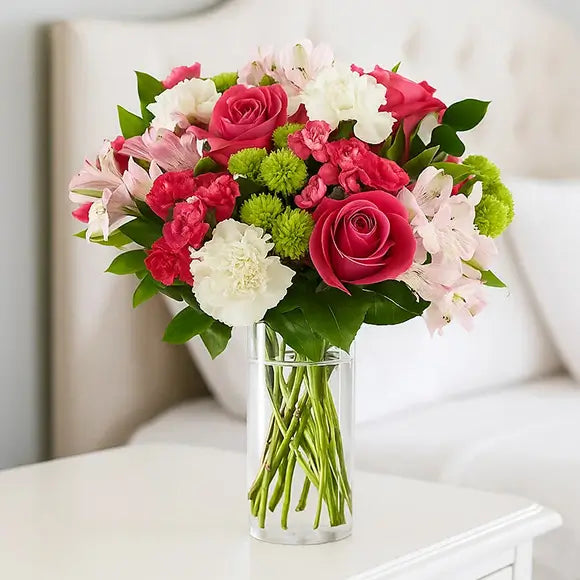 Bouquet of pink, white, and green flowers in a clear vase on a bedside table