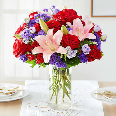 Bouquet of red, purple, and pink flowers in a clear vase on a table