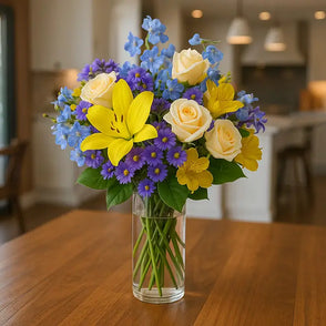 Yellow lilies, roses, and other flowers in a clear vase on a table
