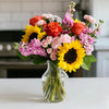 Bouquet of sunflowers and other pink and orange flowers in a clear vase.