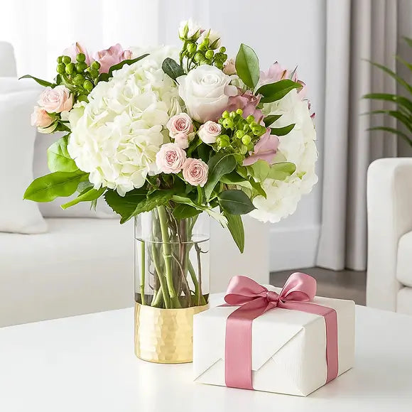 Bouquet of pink and white flowers in a vase with a present  on a table
